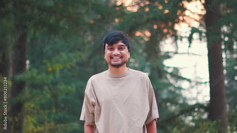 Portrait of a happy Indian man staring at the camera and smiling while standing in the middle of the pine tree forest at Manali in Himachal Pradesh, India. Tourist smiles while looking at camera. Portrait of a happy Indian man staring at the camera and smiling while standing in the middle of the pine tree forest at Manali in Himachal Pradesh, India. Tourist smiles while looking at camera.