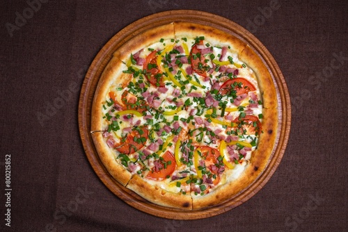 Freshly baked pizza on a wooden board, top view. Isolated on brown background.