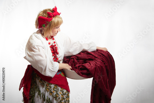 Portrait of heerful funny adult mature woman solokha washing clothes in a basin. Female model in national ethnic Slavic style. Stylized Ukrainian, Belarusian or Russian woman in comic photo shoot