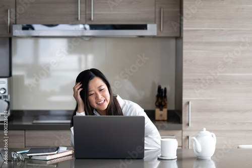 Young Asian professional woman working from home on her laptop while sipping a hot drink.