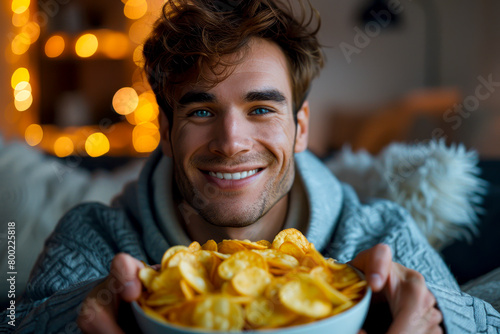 Movie Night Vibes: Young Man Enjoying Potato Chips on Sofa in Front of TV photo