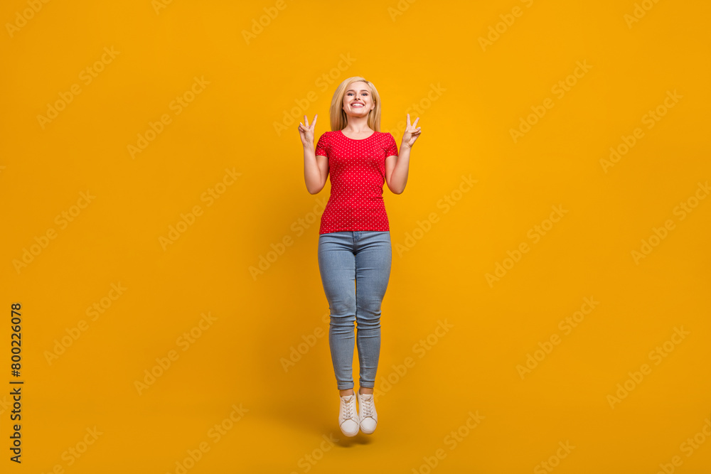 Full length body size photo woman jumping up showing v-sign isolated vibrant orange color background Full length body size photo woman jumping up showing v-sign isolated vibrant orange color background