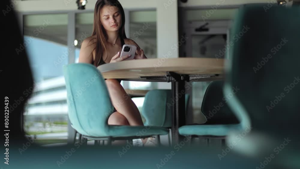 Attractive brunette girl sitting at the table and posing for the camera with phone in hands, beautiful smile, sports girl, sportswear, health, model, waiting, well-groomed girl, success, casual Attractive brunette girl sitting at the table and posing for the camera with phone in hands, beautiful smile, sports girl, sportswear, health, model, waiting, well-groomed girl, success, casual