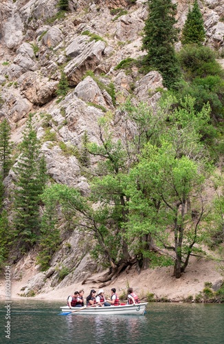 Scenic Mountain Lake with Rocky Cliffs, Forest, Boat, and Tourists on Water