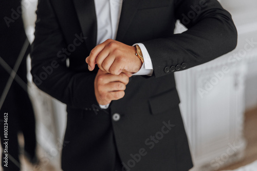 A man in a suit is wearing a gold watch and adjusting his cuff. Concept of formality and attention to detail, as the man takes care to ensure his appearance is polished and professional