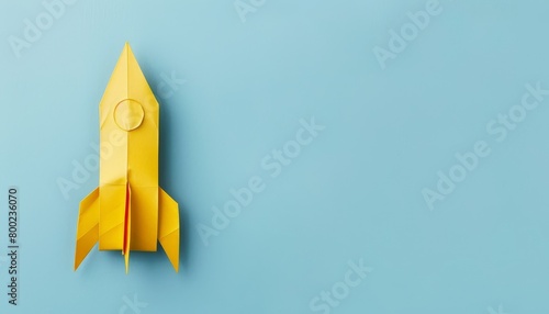 Handmade yellow paper rocket on light blue background with text space origami art