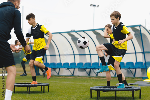 Group of young boys in sports soccer club practicing on jumping trampoline. Teenagers on football training trampoline. Youth athletes improving stability skills with young coach. Boys agility practice