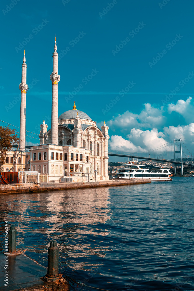 Naklejka premium A mosque with a blue sky in the background. Ortakoy Mosque, Besiktas Turkey. A mosque in Istanbul with the bridge in the background.