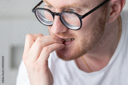 Portrait of brooding man in glasses chewing on his fingernails. Fingernail biting.