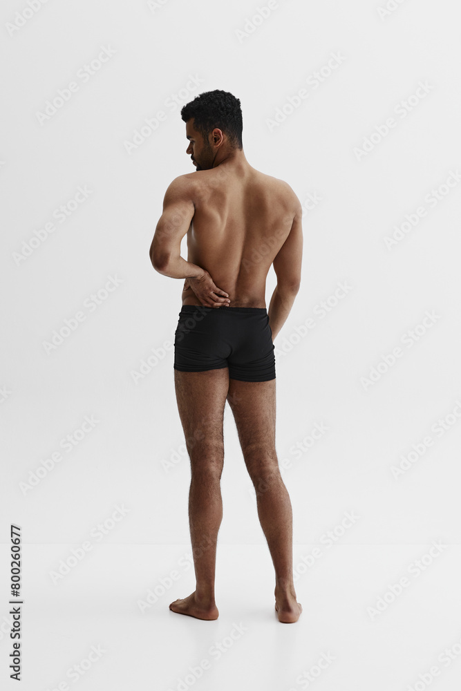 Fototapeta premium Back view. Young African-American man with relief strong back, muscular body standing in boxers isolated on white background. Back pain reduction. Concept of sport, body care, health, fitness