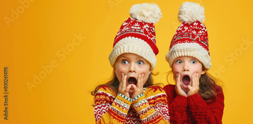 two little girl in christmas sweater and hat with hands on mouth, yellow background, banner for social media post