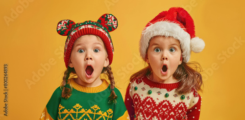 two little girl in christmas sweater and hat with hands on mouth  yellow background  banner for social media post