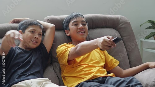 Young Boy Switch Tv Program By Remote Control and His Brother Pointing and Approve The Tv Shows. Happy Family Spending Time and Having Fun Together at Home. 
