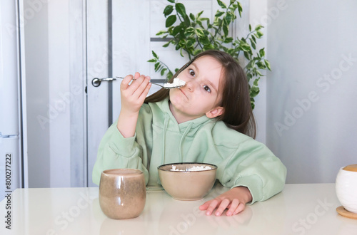Cute girl with appetite and pleasure loves to eat cottage cheese for morning breakfast, experiencing pleasure. Concept of healthy nutrition for children. Delicious food and tasty food concept