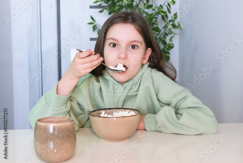 Cute girl with appetite and pleasure loves to eat cottage cheese for morning breakfast, experiencing pleasure. Concept of healthy nutrition for children. Delicious food and tasty food concept