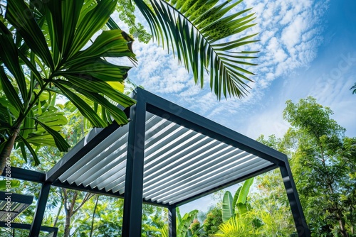 Modern louring canopy with white slats, set against the backdrop of blue sky and lush greenery. photo