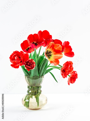 A bouquet of lush red tulips in vintage glass vase on the table on light grey background. Business card of flower shop with copy space. Invitation postcard. International women's day. Valentine's day