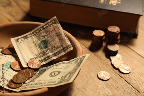 Donate and give concept. Bowl with coins, dollar banknotes and Bible on wooden table, closeup