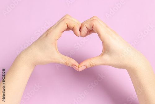 Woman showing heart gesture with hands on pink background  closeup