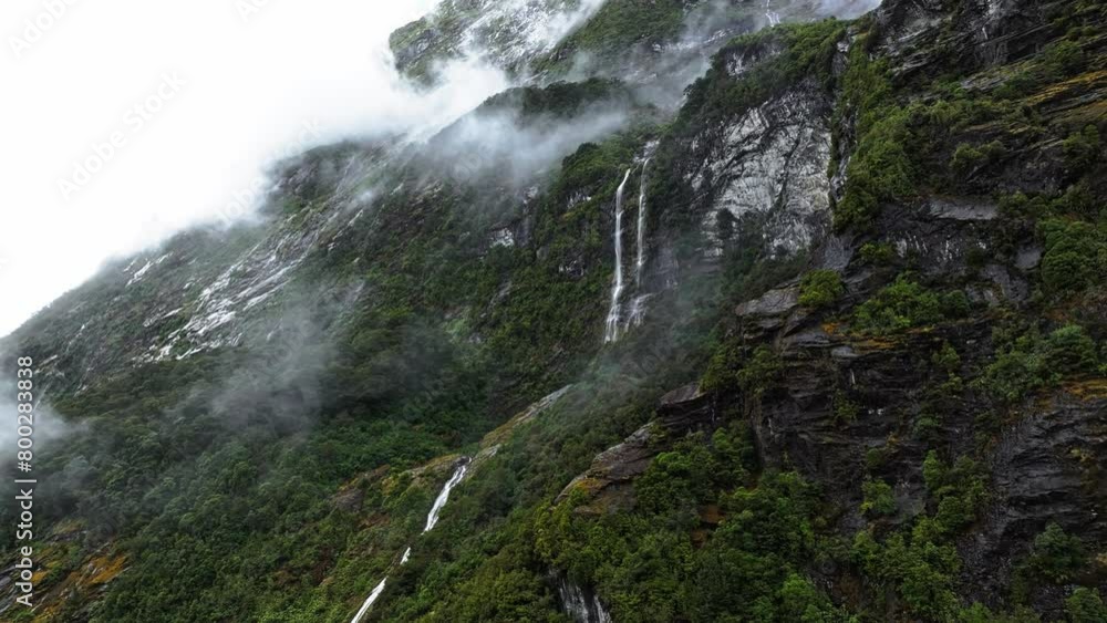 Waterfalls cascade along cliff edges of Milford Sound with low clouds above forest Waterfalls cascade along cliff edges of Milford Sound with low clouds above forest