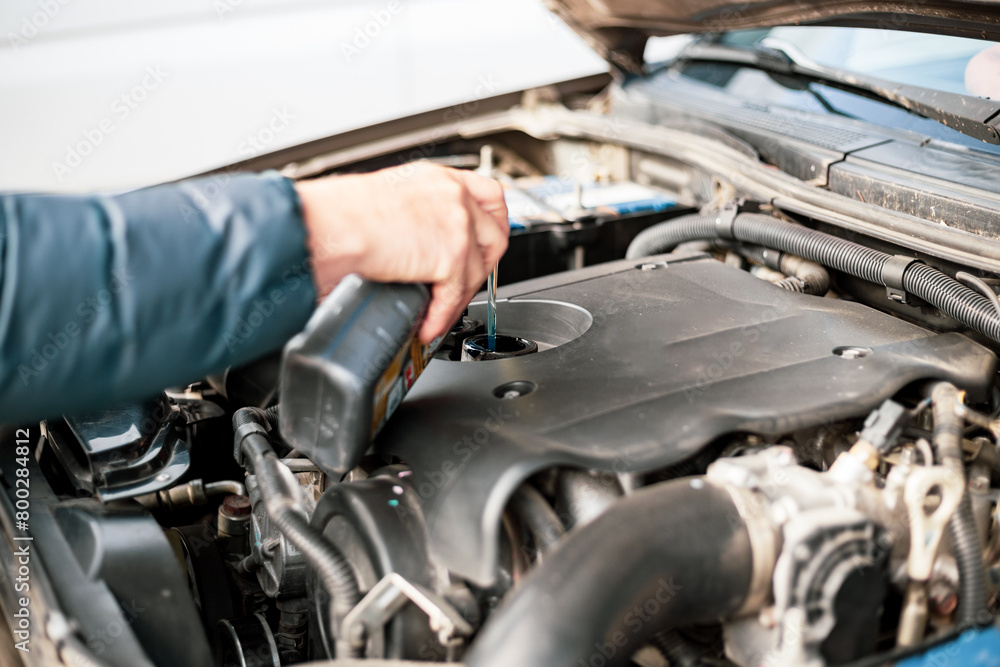 A man pours motor oil into a car engine. Changing and adding oil, car maintenance A man pours motor oil into a car engine. Changing and adding oil, car maintenance