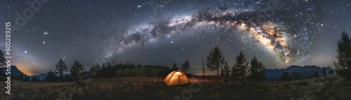 Starry night sky over a lit camping tent and a lone tree in a grassy field