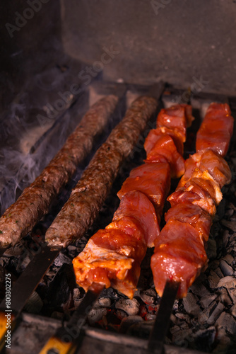 Close-up of an appetizing kebab or shashlik made of fresh meat and lula kebab is cooked on a charcoal grill with smoke. Vertical photo
