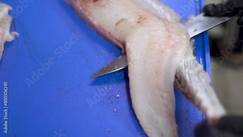 Chef hands with black gloves skinning fish fillet with a Sharp knife on a blue cutting board. Close-up. Cleaning fish with a kitchen knife. Traditional food preparation. photo