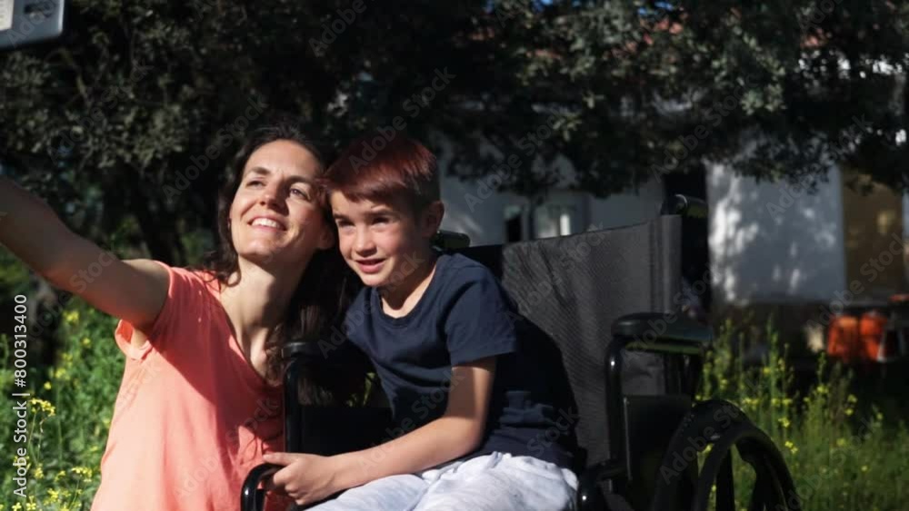 Mother with her son in a wheelchair taking a selfie with her cell phone in nature in spring Mother with her son in a wheelchair taking a selfie with her cell phone in nature in spring