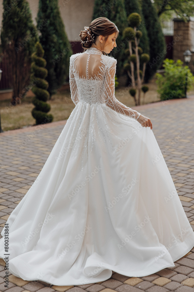 A woman in a long white dress is standing in front of a brick wall. She is wearing a necklace and her hair is pulled back A woman in a long white dress is standing in front of a brick wall. She is wearing a necklace and her hair is pulled back