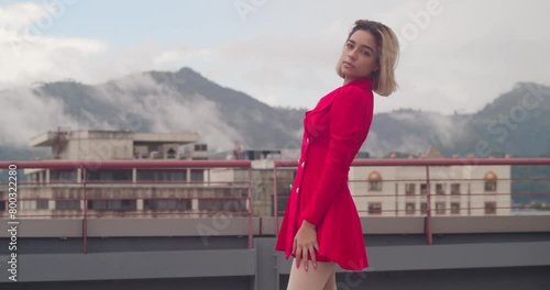 A short red dress adorns a young Hispanic girl as she gazes out from the city rooftop. photo