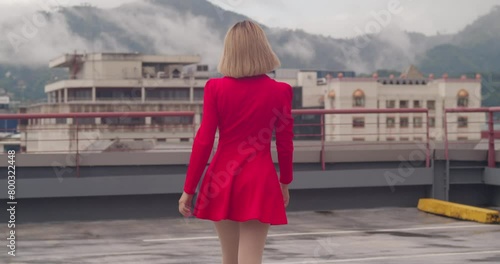 A rooftop in the bustling city becomes the stage for a young Hispanic girl, walking adorned in a short red dress. photo