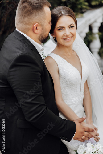 A bride and groom are posing for a picture. The bride is wearing a white dress and the groom is wearing a black suit. They are both smiling and looking at the camera © Vasil
