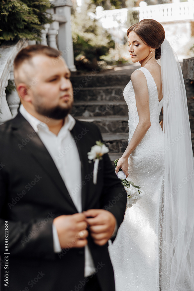 A man and a woman are posing for a picture. The man is wearing a black suit and the woman is wearing a white dress. The man is holding a bouquet of flowers in his hand A man and a woman are posing for a picture. The man is wearing a black suit and the woman is wearing a white dress. The man is holding a bouquet of flowers in his hand
