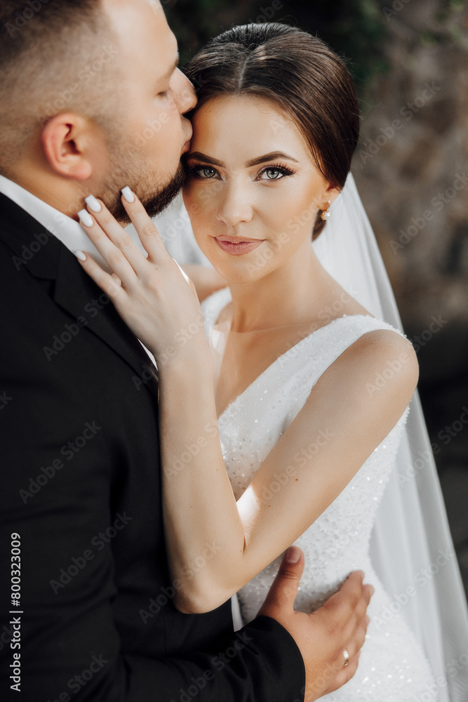 A bride and groom are hugging each other, with the bride wearing a white dress. The man is kissing the woman's lips A bride and groom are hugging each other, with the bride wearing a white dress. The man is kissing the woman's lips