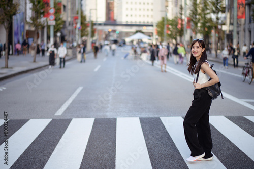 Explore urban vibes with a happy Asian woman at a city crosswalk, showcasing a mix of style, joy, and the pulse of local life.