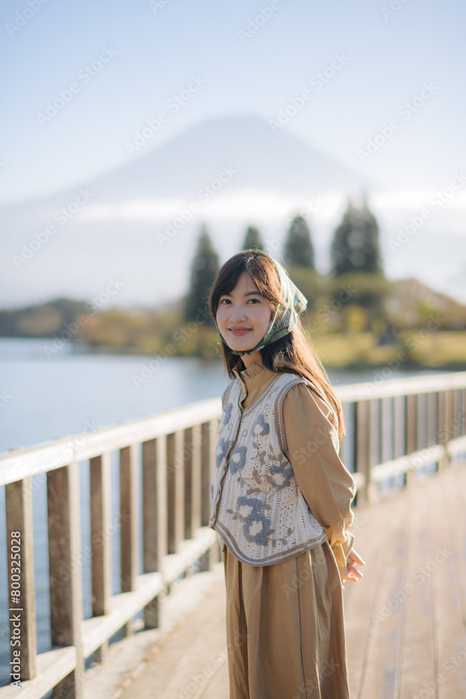 Experience the joy of a vacation: Asian woman in a casual dress takes in the stunning scenery of Mount Fuji, capturing sunny morning and the serene beauty of Kawaguchiko Lake.