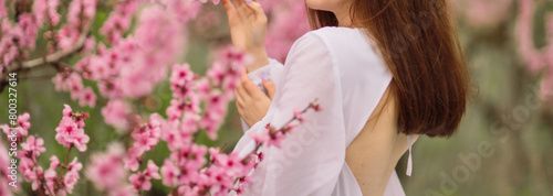 A girl is walking through a field of pink peach flowers. She is wearing a white dress and carrying a basket. The scene is peaceful and serene, with the pink flowers creating a beautiful