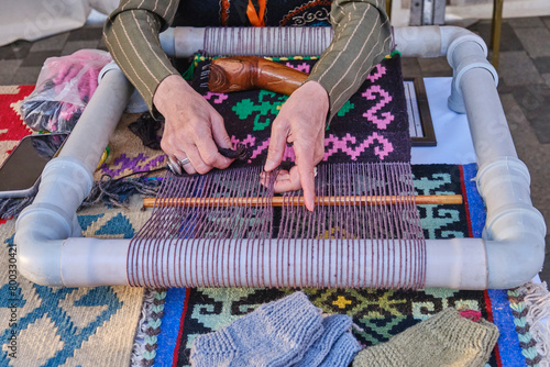 Hands of senior woman weaves a carpet with traditional asian pattern on handloom