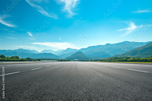 Empty asphalt under a blue sky and rolling mountains in the distance