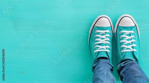   A tight shot of feet clad in blue Converse shoes, sporting white laces, against a turquoise backdrop photo