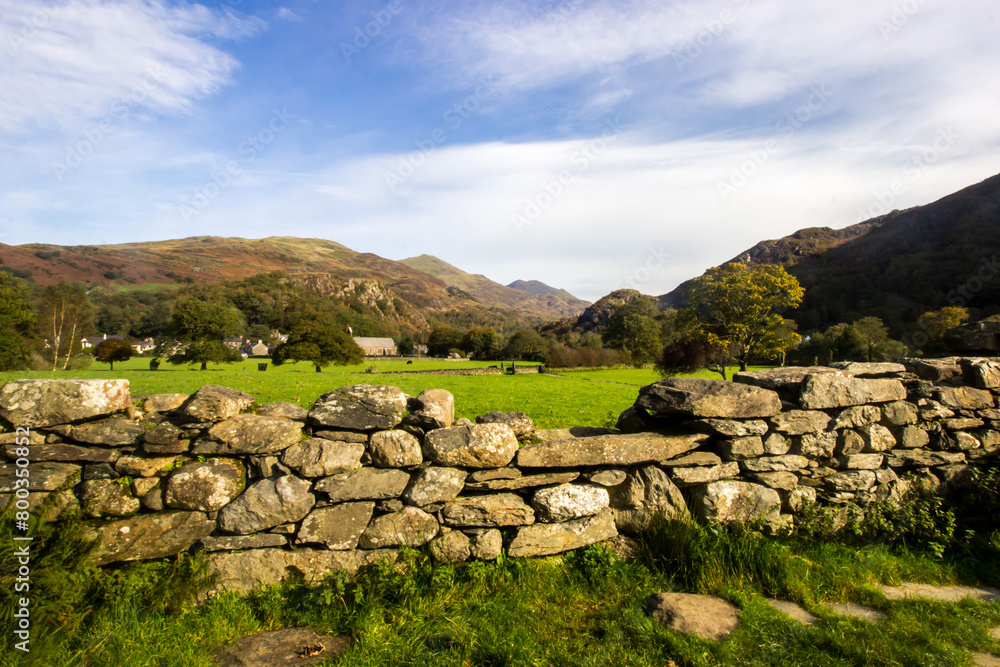 Picturesque view towards the Welsh village of Beddgelert, over the broken wall of a ruin, with the peaks of Dinas Emrys and Ed Wyddfa rising in the background