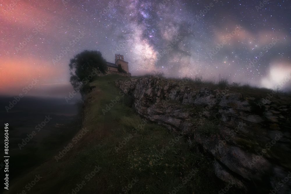 night view of the Church of San Pantaleon de Losa, in Las Merindades, Burgos, with the Milky Way shadowing the church in a sky with clouds and stars
