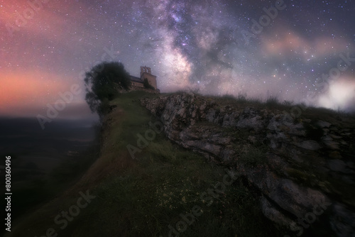 night view of the Church of San Pantaleon de Losa, in Las Merindades, Burgos, with the Milky Way shadowing the church in a sky with clouds and stars photo
