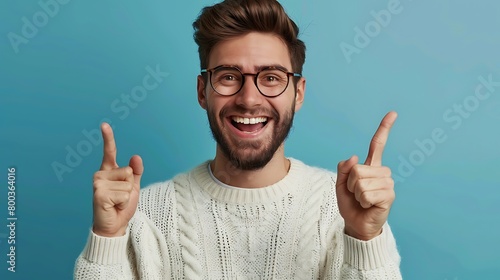 A Young handsome man with beard wearing casual sweater and glasses over blue background Smiling with open mouth, fingers pointing and forcing cheerful smile photo