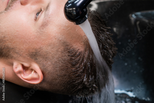 Hairdresser washes man hair from shampoo with warm water in barbershop closeup. Barber takes care of male client hair in professional salon