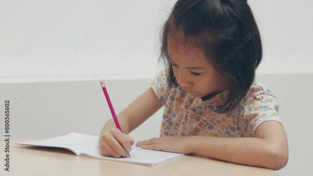 Half body with copy space of adorable Asian kid girl who is writing with determination and concentrating on notebook shows concept of education and studying of child in classroom for school student. Half body with copy space of adorable Asian kid girl who is writing with determination and concentrating on notebook shows concept of education and studying of child in classroom for school student.