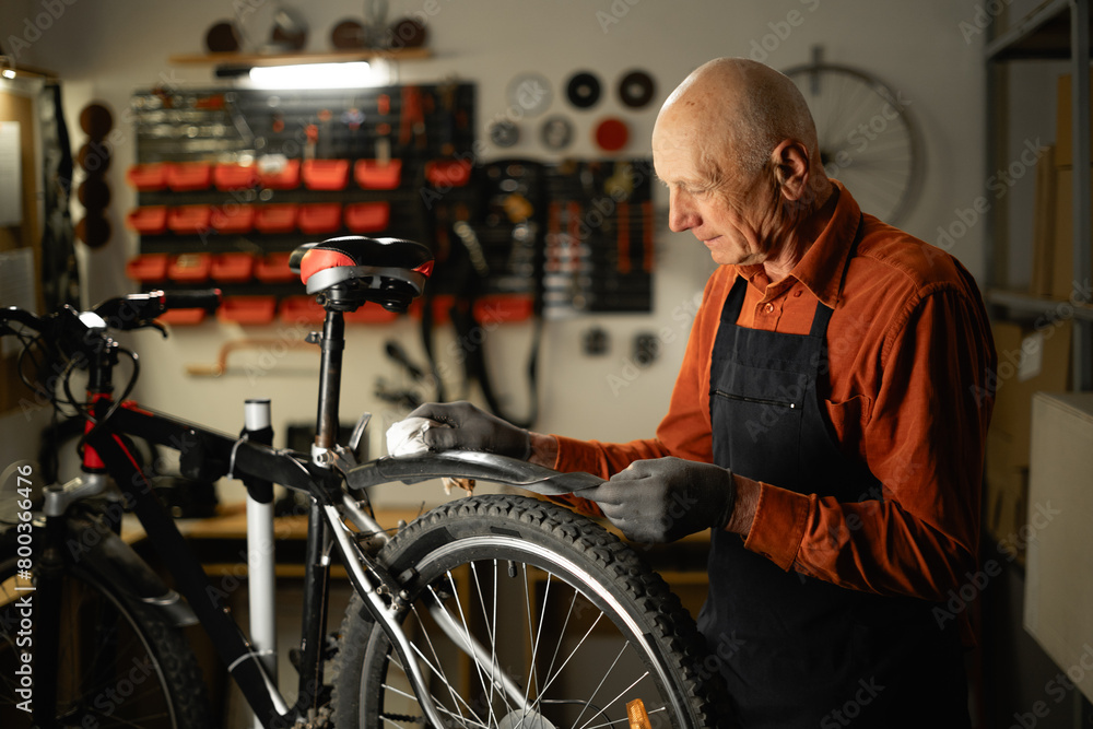 Obraz premium Bicycle Maintenance Concept. Old male mechanic or repairman working in a motorcycle repair garage, cleaning a wheel from dust.