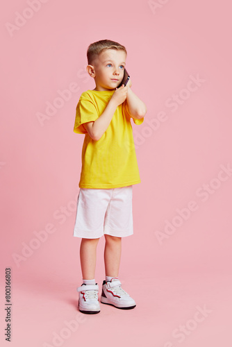 Little child, dressed casual talking on phone against pink studio background. Perfect cellular connection. Concept of fashion and style, beauty, back to school, childhood, technology. Ad