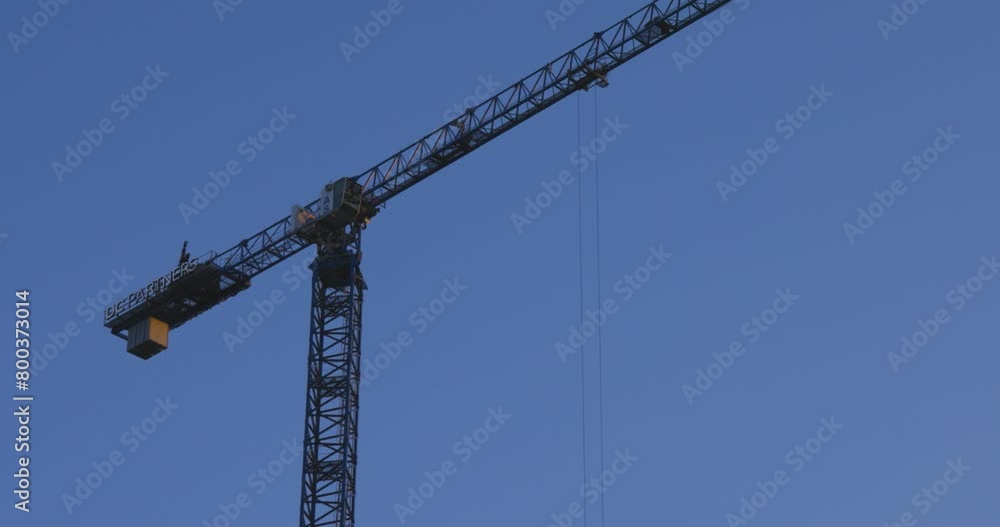 Low angle lockdown shot of tall crane turning against clear blue sky during daytime Low angle lockdown shot of tall crane turning against clear blue sky during daytime